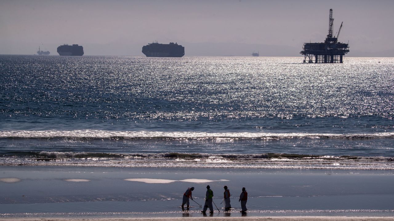 Container ships and an oil derrick line in the horizon as environmental oil spill cleanup crews search Huntington Beach on October 5, 2021, cleaning up oil chucks from the oil spill