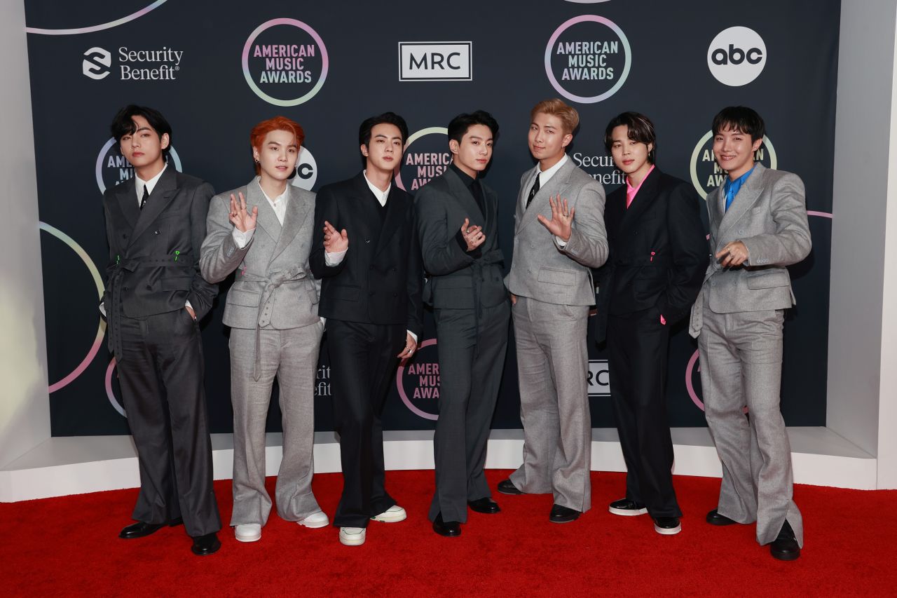 K-Pop group BTS arrived as a cohesive unit in shades of grey and charcoal, donning double-breasted Louis Vuitton suits with tie belt details and small pops of color in pink, blue and green.
