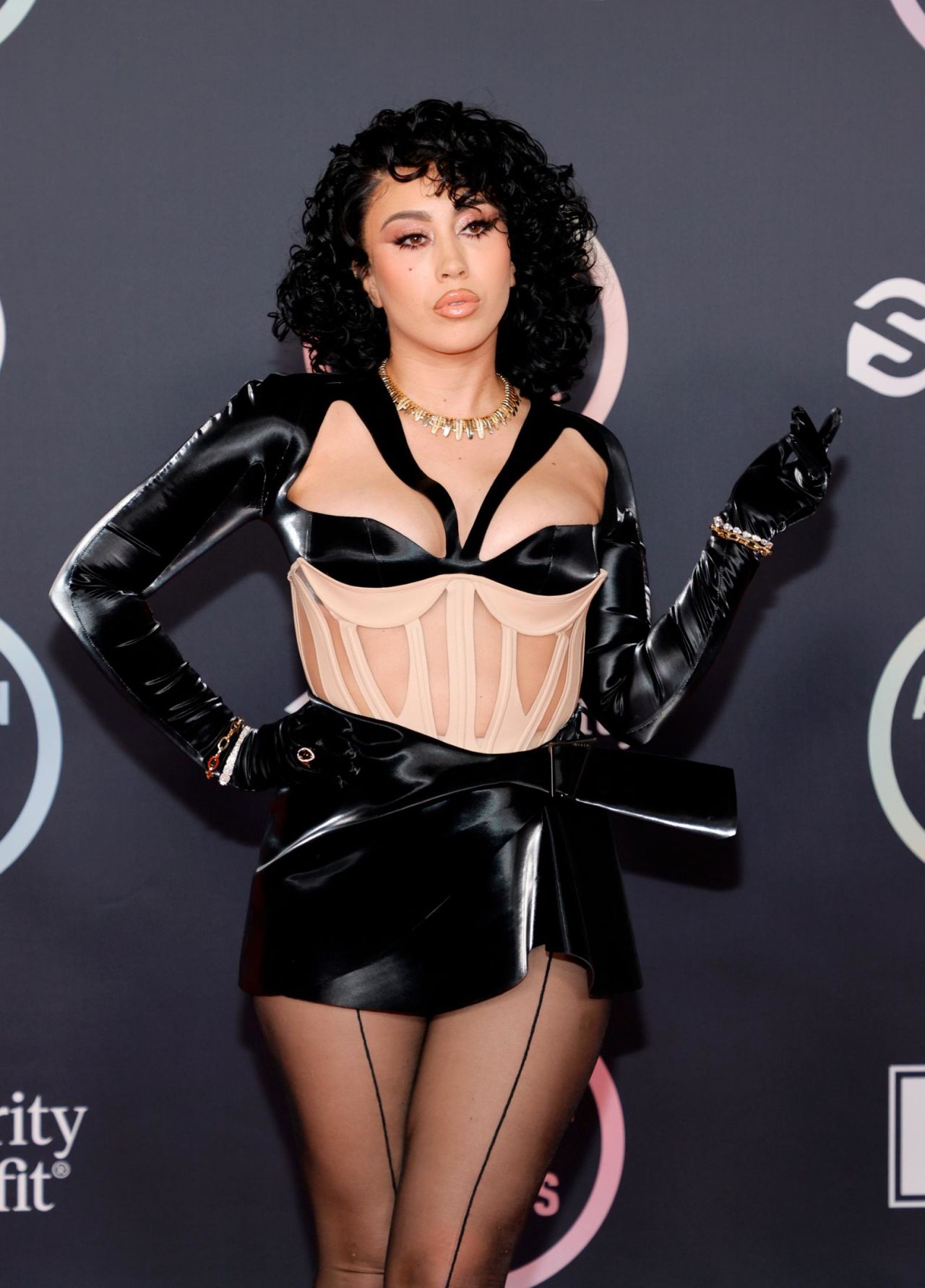 Kali Uchis wore not just one, but two corseted outfits on the AMAs' red carpet. The above is Uchis' second outfit, a Thierry Mugler ensemble featuring black glossy mini skirt, long gloves and a sheer corset with boning and contrasting cups. 