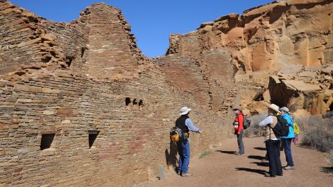 A guide leads a group of visitors through the ruins of a massive stone complex (Pueblo Bonito) at Chaco Culture National Historical Park in northwestern New Mexico. The communal stone buildings were built between the mid-800s and 1100 A.D.