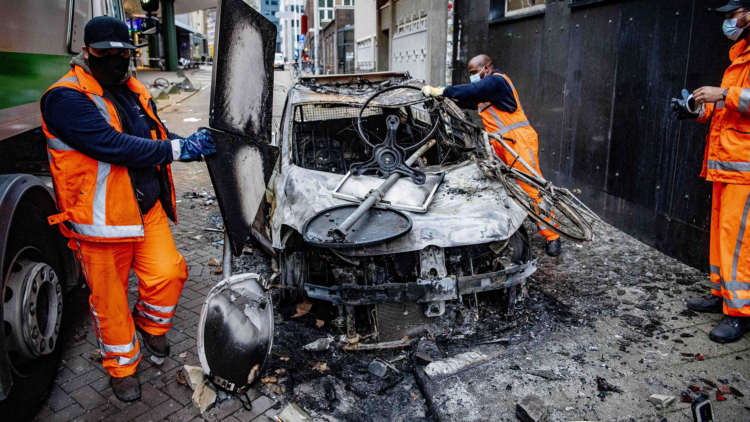 Workers clear debris from a damaged car in Rotterdam, Netherlands, on Saturday, November 20. There were violent clashes the night before as people protested against the country's new Covid-19 restrictions.