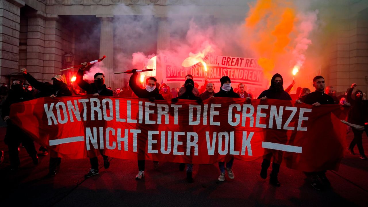 Crowds shout slogans and light flares during a demonstration against Austria's Covid restrictions. The banner reads: "Control the border. Not your people."
