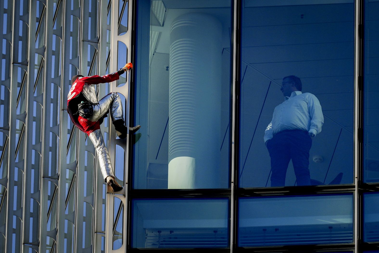 A man watches urban climber Alain Robert scale the Skyper high-rise in Frankfurt, Germany, on Tuesday, November 23.