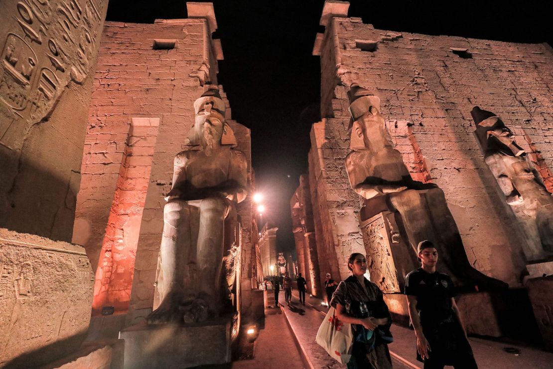 Visitors walk past the statues of the Ancient Egyptian New Kingdom Pharaoh Ramses II at night.