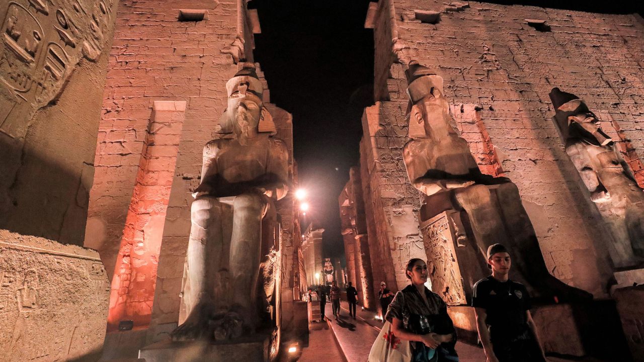 Visitors walk past the statues of the Ancient Egyptian New Kingdom Pharaoh Ramses II at night.