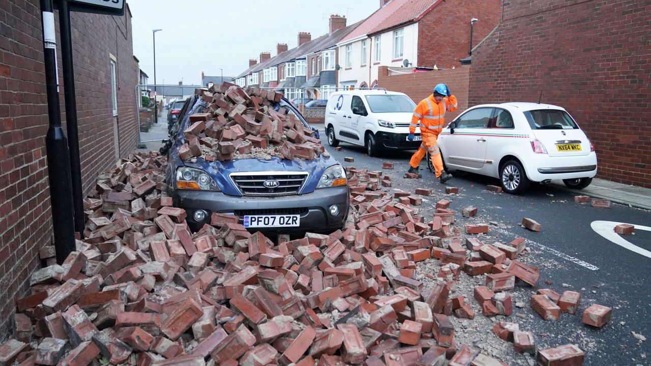 A man walks past a car lying under fallen masonry from a property Sunderland, northeast England, after high winds battered some areas of the country.