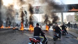 Lebanese men drive bikes past burning tyres set up by protesters to block a road in the capital Beirut on November 29, 2021, as the country struggles with a deep economic crisis. 