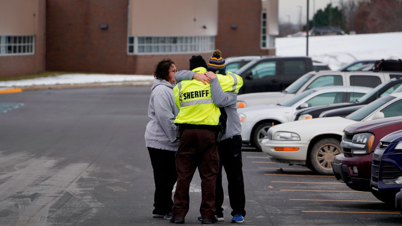 An Oakland County Sheriff's deputy hugs family members of a student in the parking lot of Oxford High School in Oxford, Mich., Wednesday, Dec. 1, 2021. A 15-year-old sophomore opened fire at the school, killing several students and wounding multiple other people, including a teacher.