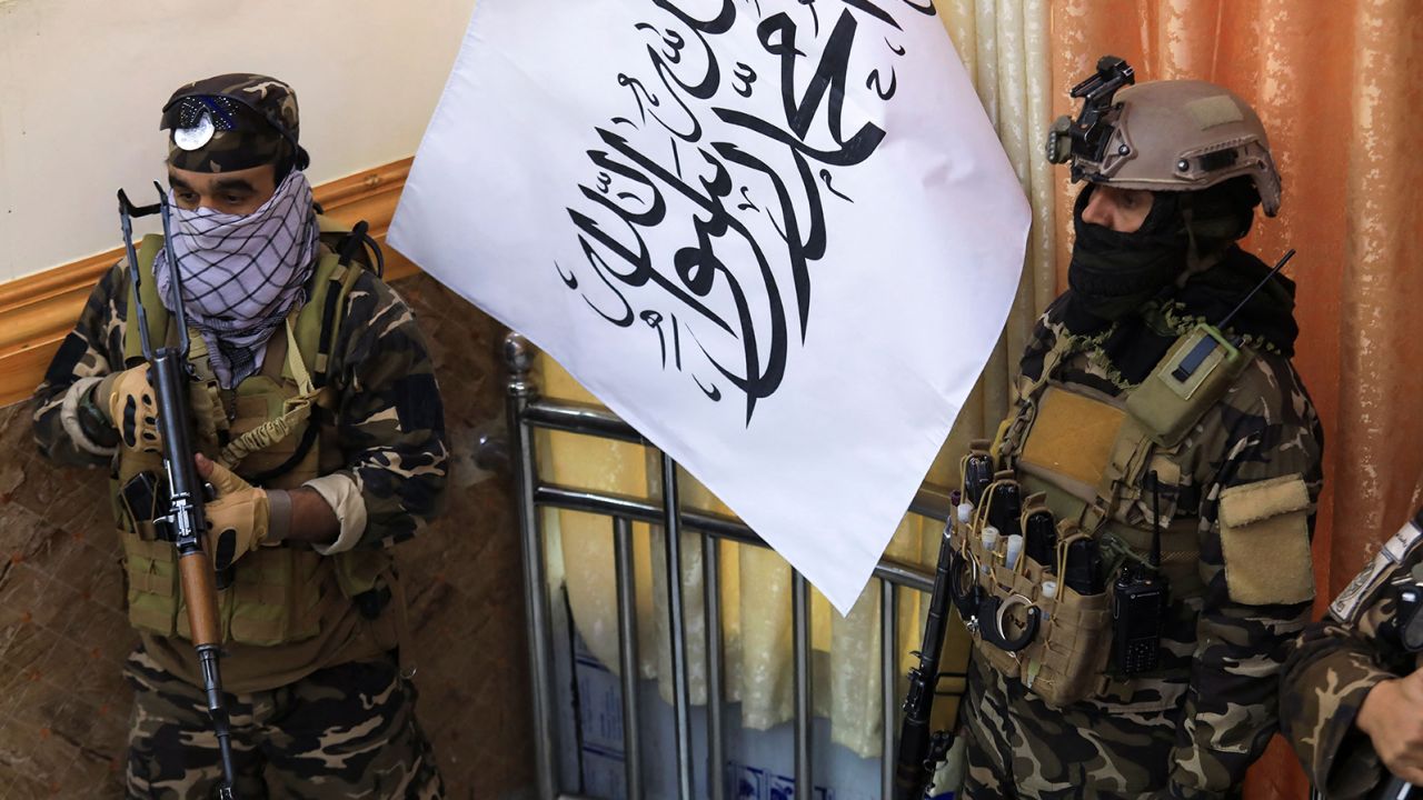 Taliban fighters stand guard next to a Taliban flag during a gathering where Afghan Hazara elders pledged their support to the country's new Taliban rulers, in Kabul on November 25, 2021.