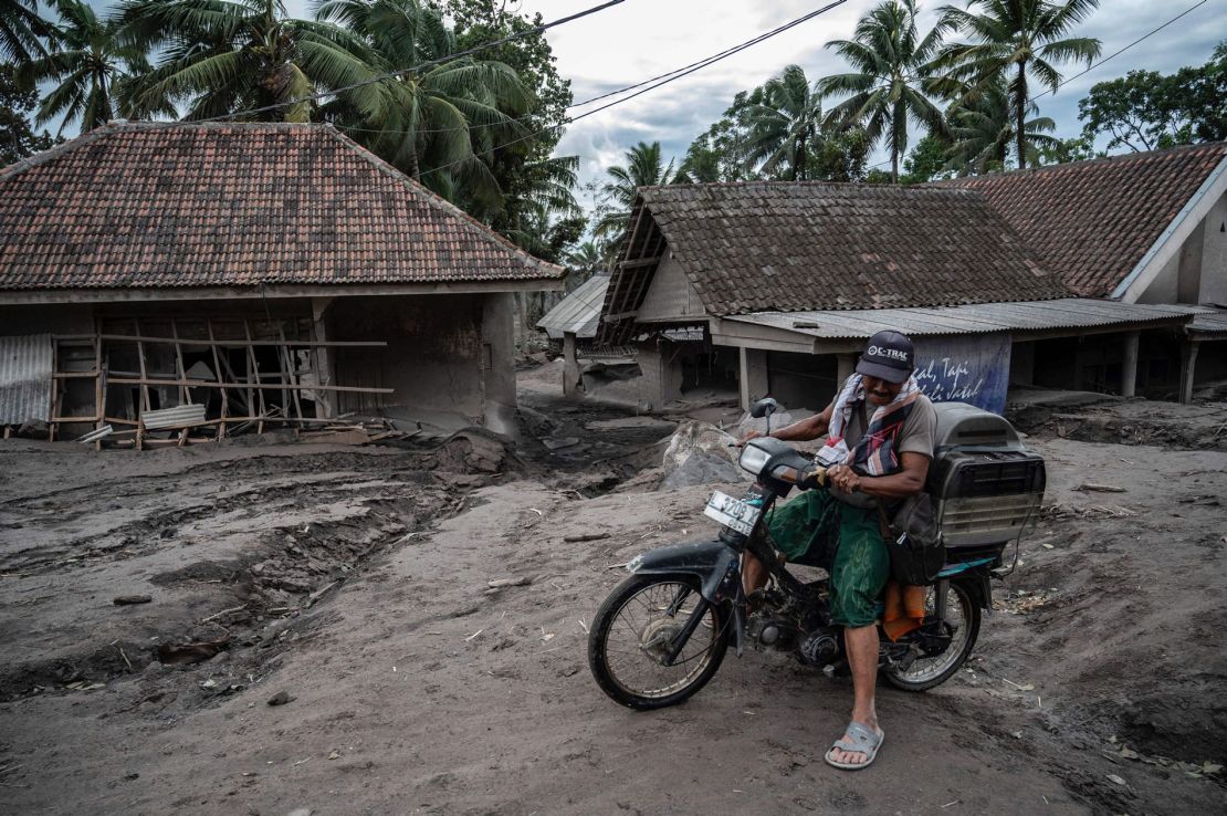 A man rides a bike past damaged homes at Sumber Wuluh village in Lumajang on December 6, 2021.