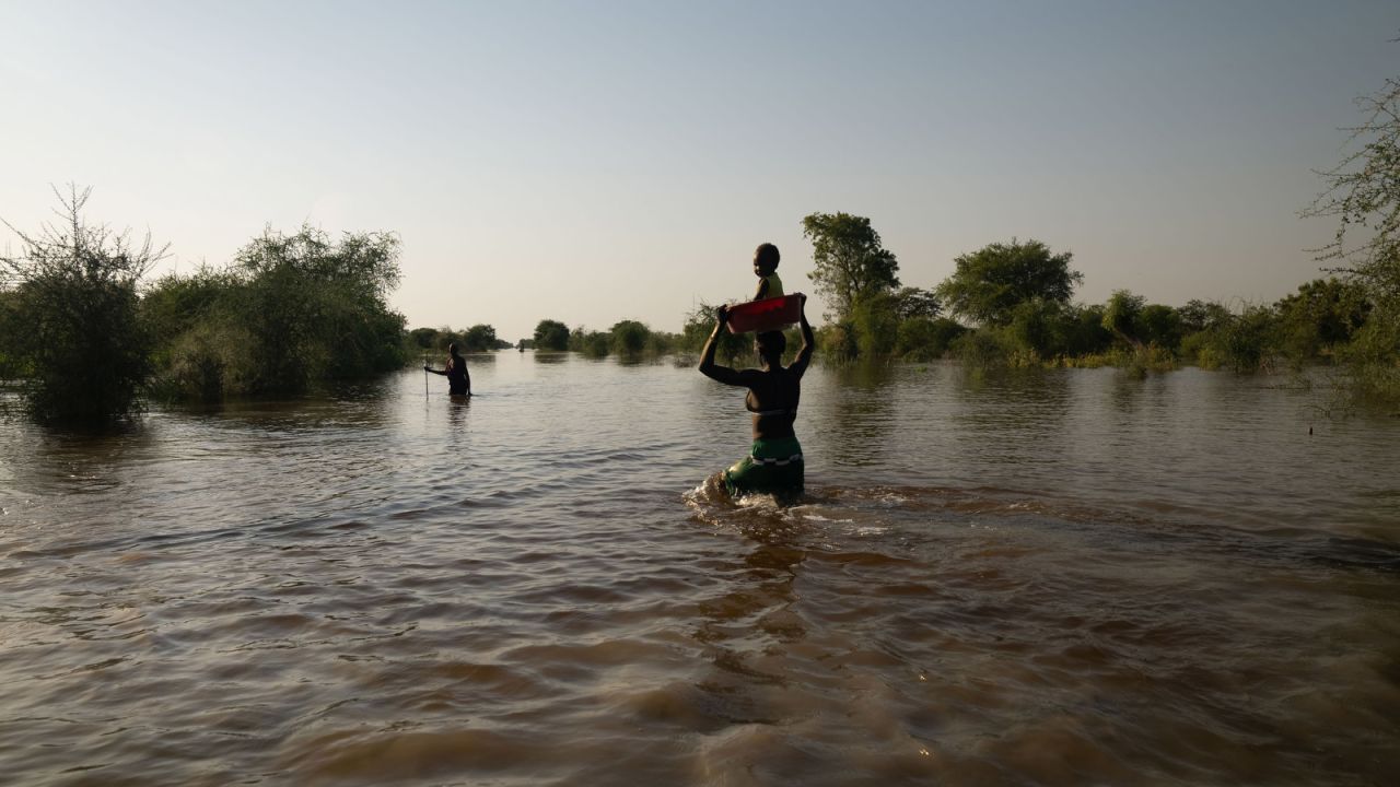 A woman carries her baby on her head as she wades through the floodwaters.