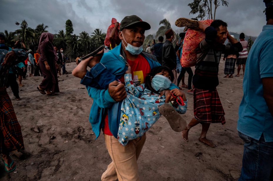 A man carries a child Sunday as other people salvage their belongings from an area covered in volcanic ash at the Sumberwuluh village in Indonesia's Lumajang district.
