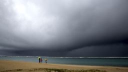 People hold umbrellas as it begins to rain on an otherwise empty beach in Honolulu on Monday, Dec. 6, 2021. A strong storm packing high winds and extremely heavy rain flooded roads and downed power lines and tree branches across Hawaii, with officials warning Monday of potentially worse conditions ahead.