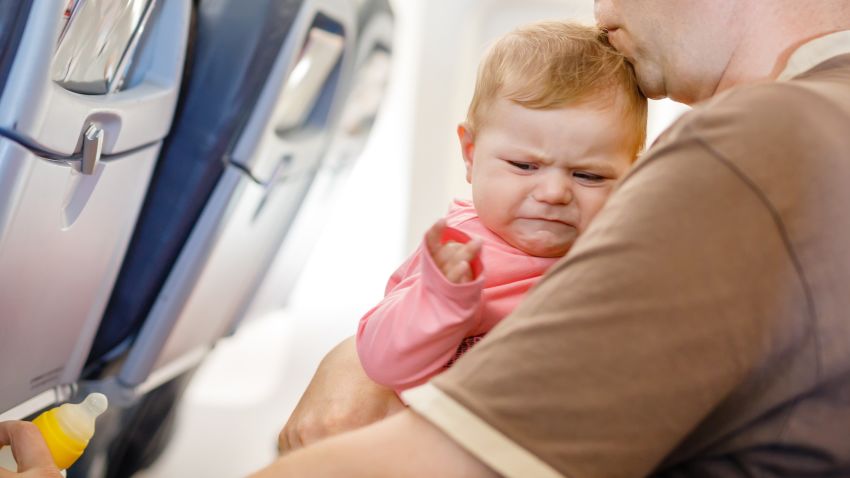 Young tired father and his crying baby daughter during flight on airplane going on vacations.