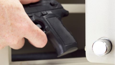 A person puts a firearm in a gun safe.