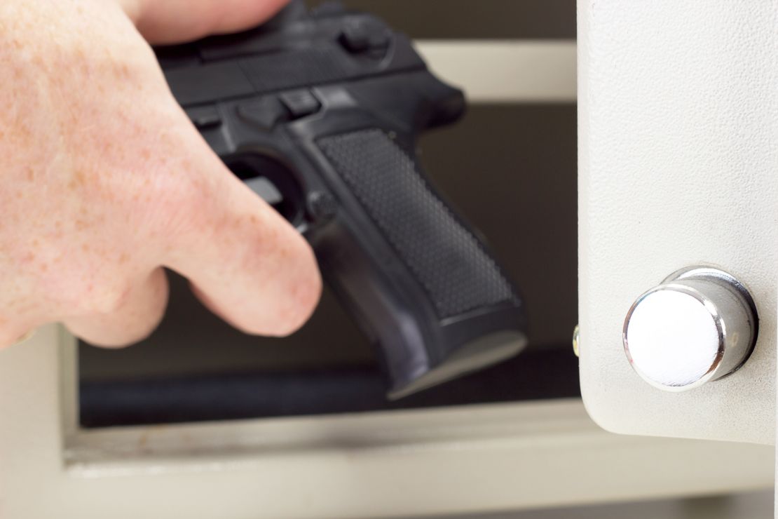A person puts a firearm in a gun safe.