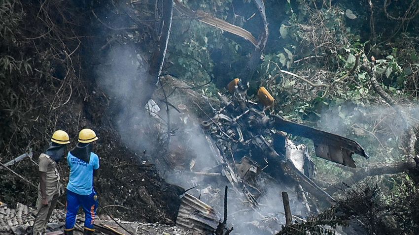 Firemen and rescue workers stand next to the debris of an IAF Mi-17V5 helicopter crash site in Coonoor, Tamil Nadu, on December 8, 2021. - A helicopter carrying India's defence chief General Bipin Rawat crashed, the air force said, with a government minister at the scene saying at least seven people were dead.