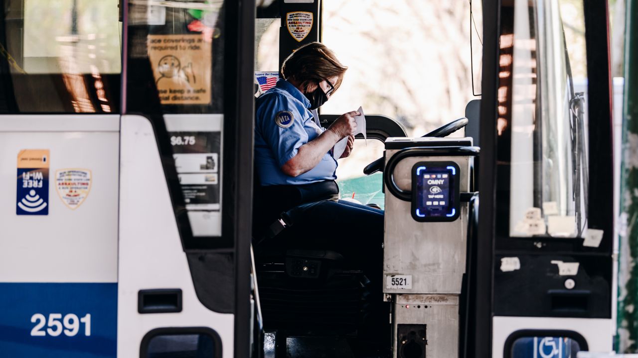 A bus driver wears a protective mask while picking up passengers at a bus stop in New York.