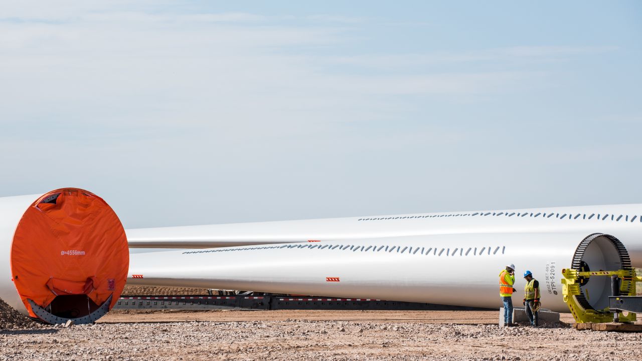 Construction workers stand in front of wind turbine blades at a wind farm in Encino, New Mexico.