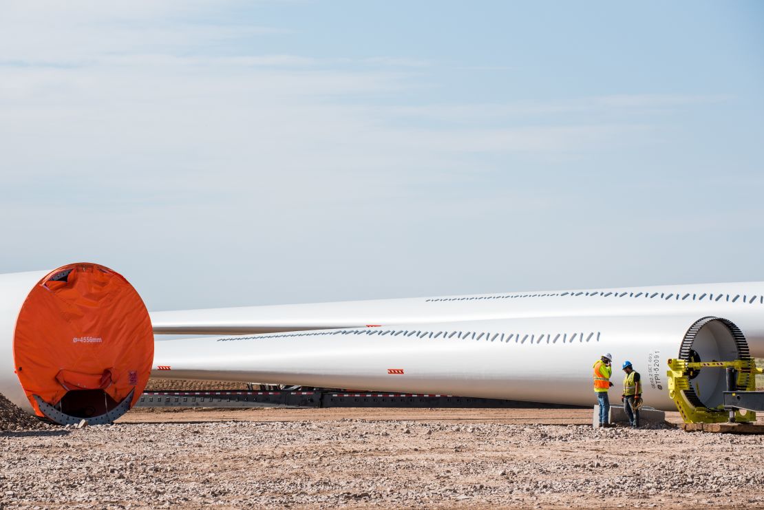 Construction workers stand in front of wind turbine blades at a wind farm in Encino, New Mexico.