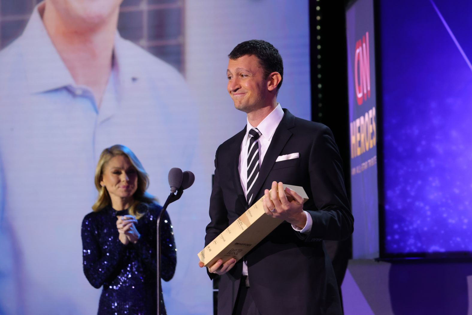 2021 CNN Hero David Flink accepts his award onstage from Kelly Ripa. Since 1998, <a href="index.php?page=&url=https%3A%2F%2Feyetoeyenational.org%2F" target="_blank" target="_blank">Eye to Eye</a> has grown into a nationwide non-profit that pairs middle school children who have a learning difference with a college or high school mentor who also has a learning difference.