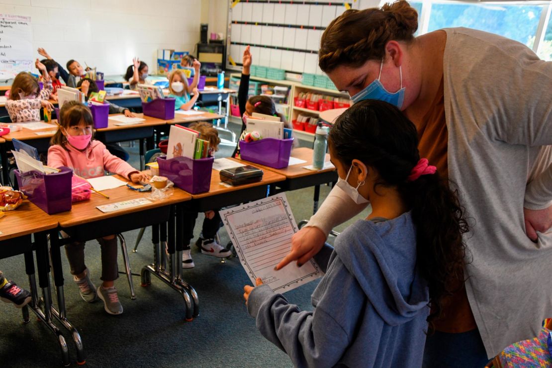 A second grade teacher at Colin L. Powell Elementary School helps a student read aloud a letter they wrote to the family of Colin Powell after his death due to Covid-19 complications.