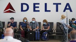 FILE - People sit under Delta sign at Salt Lake City International Airport on July 1, 2021, in Salt Lake City. Delta Air Lines won't force employees to get vaccinated, but it's going to make unvaccinated workers pay a $200 monthly charge. Delta said Wednesday, Aug. 25, 2021 that it will also require weekly testing for unvaccinated employees starting next month, although the airline says it'll pick up the cost of that testing. 