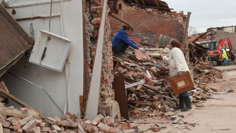 Shawna Driscoll cries as she hands unbroken ceramic plates to her friend Angee Wilson while digging through debris at Wilson's mother's tax office in Mayfield on December 15.