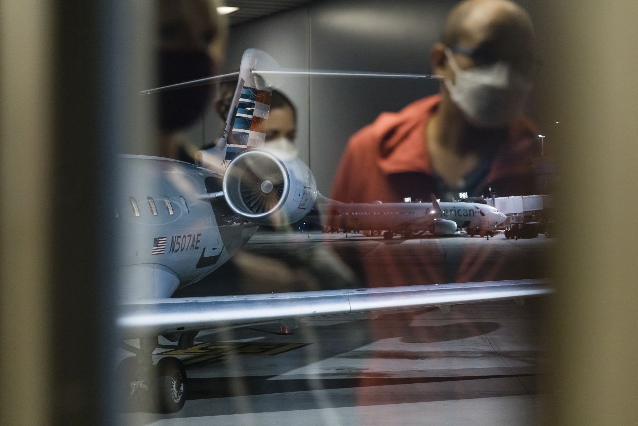 Travelers wearing protective face masks are reflected in a window at Charlotte Douglas International Airport on August 5, 2021.