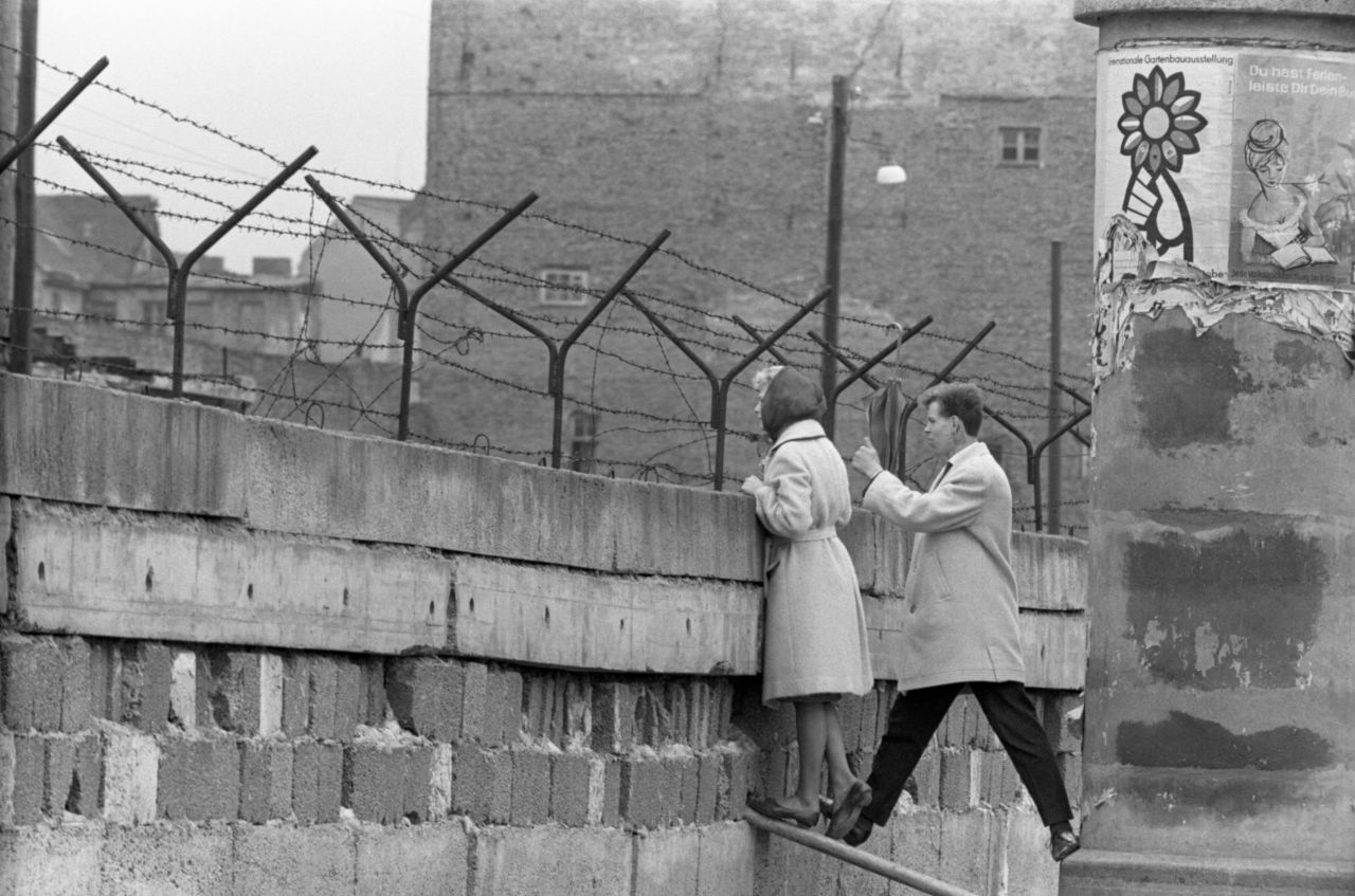 A young woman, accompanied by her boyfriend, stands at the Berlin Wall to talk to her mother on the East Berlin side in 1962. The wall divided the eastern and western sectors of the city. The US had rejected proposals by Soviet leader Nikita Khrushchev to make Berlin a "free city" with access controlled by East Germany, and in August 1961 Communist authorities began construction on the wall to prevent East Germans from fleeing to West Berlin.