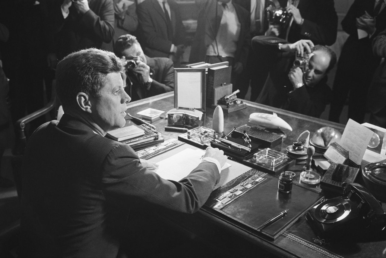 Reporters take pictures of US President John F. Kennedy behind his desk after he signed the arms embargo against Cuba in 1962. The embargo effectively quarantined Cuba. In 1961, a US-organized invasion of 1,400 Cuban exiles was defeated by Castro's forces at the Bay of Pigs. President Kennedy took full responsibility for the disaster. The next year, the Soviet Union installed nuclear missiles on Cuba capable of reaching most of the US. Kennedy ordered a naval blockade of Cuba until the Soviets removed the missiles. Six days later, the Soviets agree to remove the missiles, defusing one of the most dangerous confrontations of the Cold War.