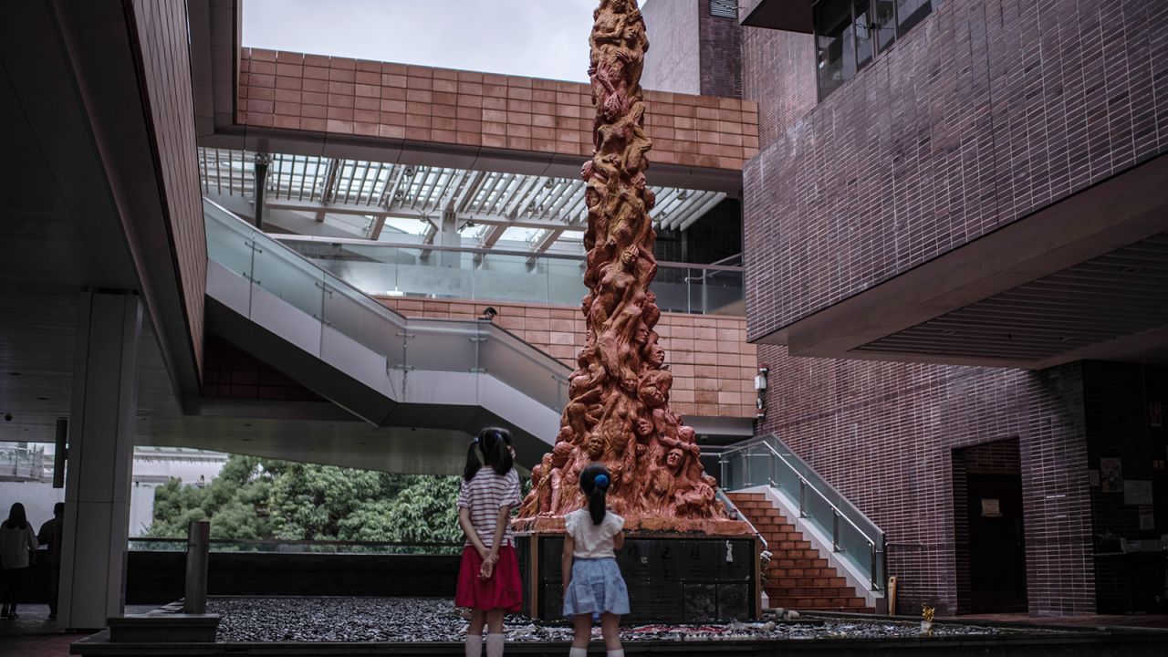 HONG KONG, CHINA - OCTOBER 15: Two children look at the "Pillar of Shame" statue at the Hong Kong University campus on October 15, 2021 in Hong Kong, China. Hong Kong University demanded that a now-disbanded pro-democracy alliance remove the artwork, an eight-metre tall monument to the Tiananmen Square Massacre by Danish artist Jens Glaschiot, after it has stood on the grounds of the campus for 24 years, local news sources reported. The statue is an iconic art piece, one of several by the artist placed around the world commemorating similar events. (Photo by Louise Delmotte/Getty Images)
