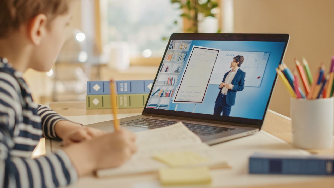 Smart Little Boy Uses Laptop for Video Call with His Teacher. Screen Shows Online Lecture with Teacher Explaining Subject from a Classroom. E-Education Distance Learning, Homeschooling. Over Shoulder