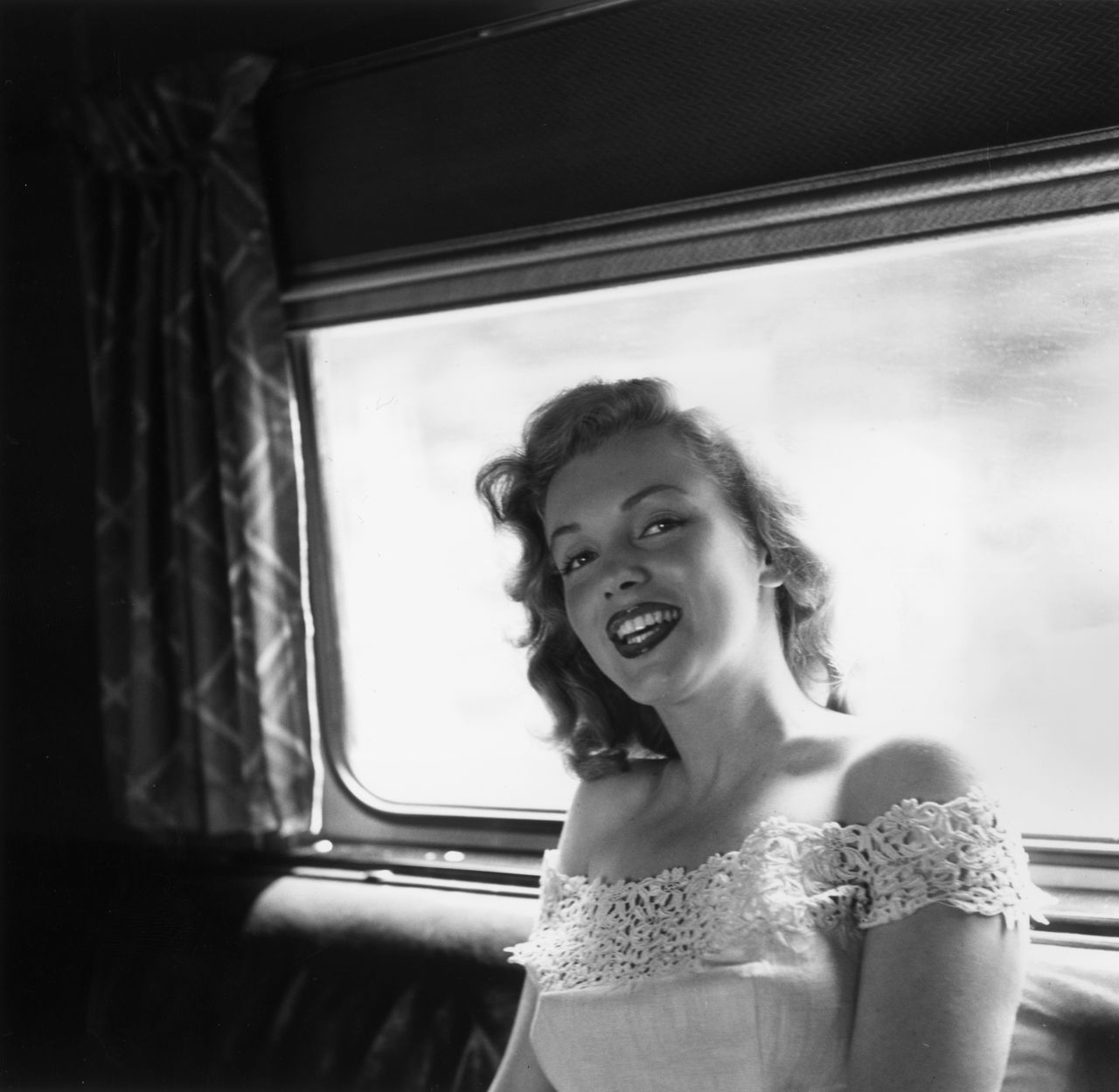 Monroe is seen sitting on a train to Warrenburg, New York, to present the keys to a new house to a winner of a Photoplay Magazine contest in 1949. Photoplay Magazine was an American film fan magazine. Monroe was on the cover in 1953.