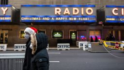 A person wearing a Santa Claus hat and a mask walks past an empty street and Radio City Music Hall which is closed due to rising cases of COVID-19 on December 23, 2021 in New York City. Radio City Music Hall announced on December 17 that they would be canceling all performances for the rest of the season. The annual Radio City Christmas Spectacular draws large numbers of crowds and tourism into the area and New York City.  