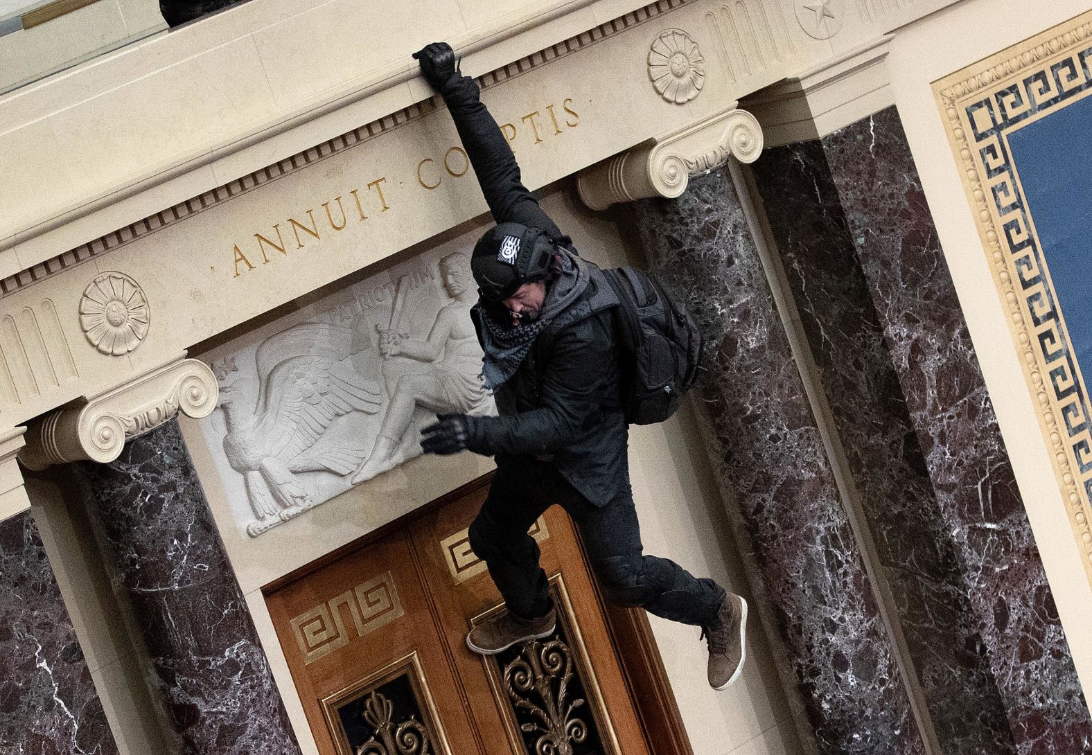 A man hangs from a balcony in the Senate chamber.