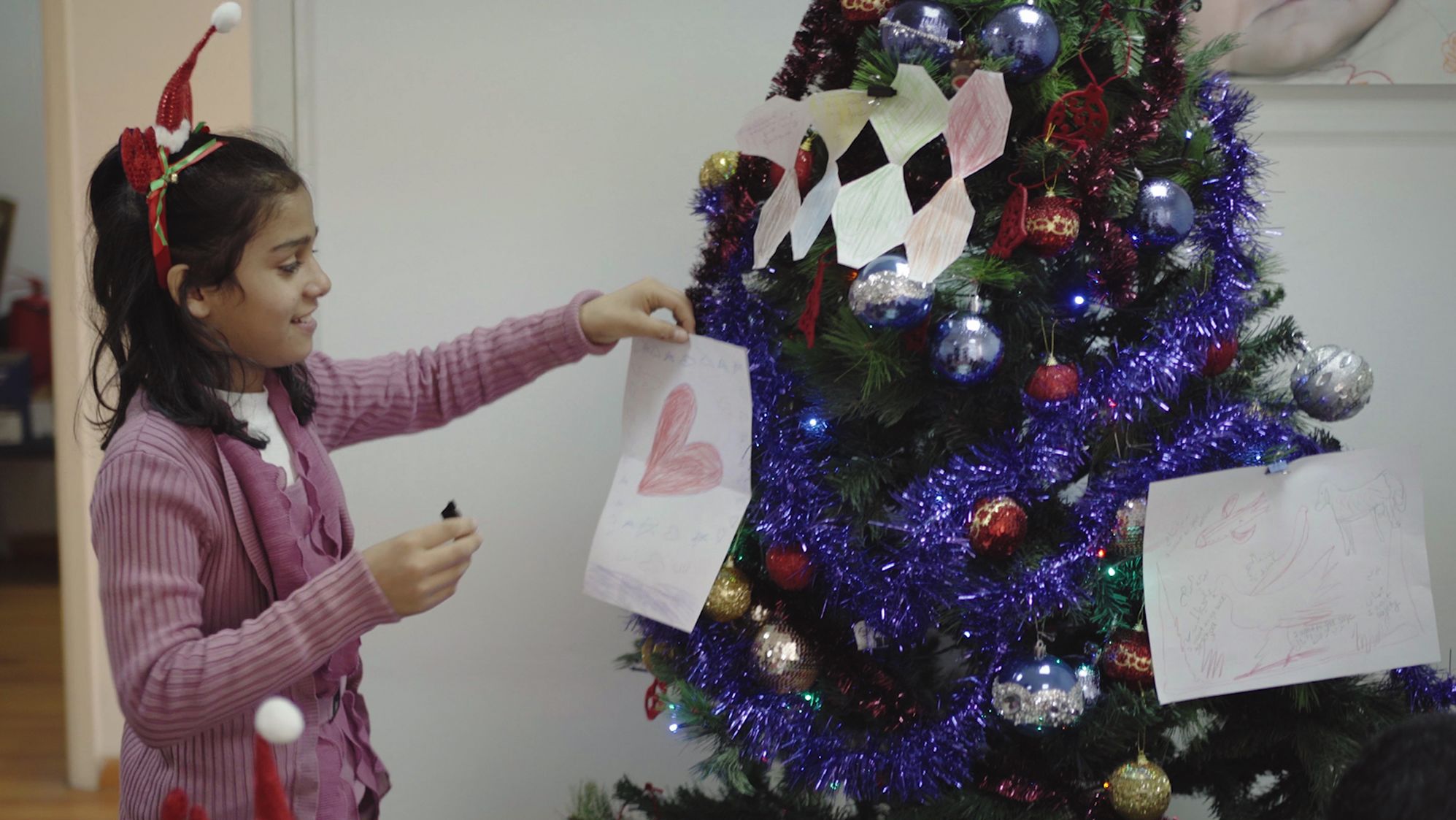 One of INARA's children places a decoration she made with her holiday wishes written on it onto a Christmas tree.