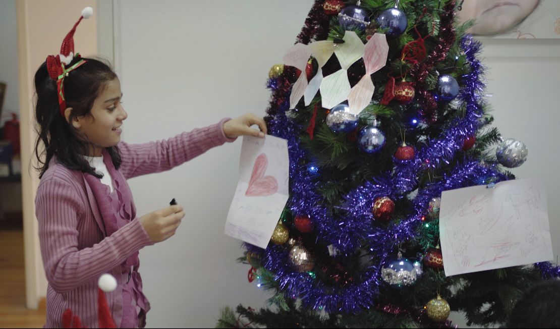 One of INARA's children places a decoration she made with her holiday wishes written on it onto a Christmas tree.
