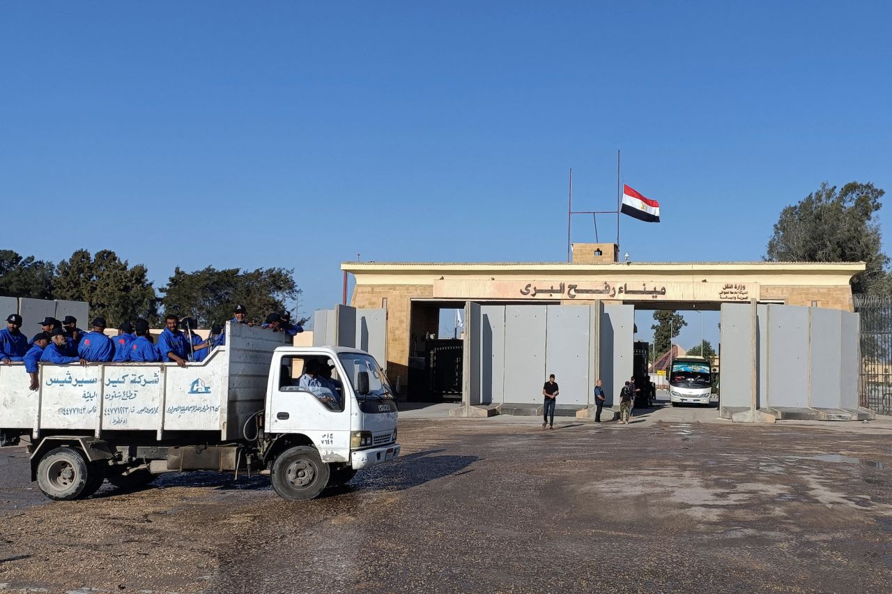 Egyptian cleaning workers are seen in front of the Rafah Crossing from the Egyptian side, while trucks carrying humanitarian aid for Palestinians await for it to open to enter Gaza in Rafah on Thursday.