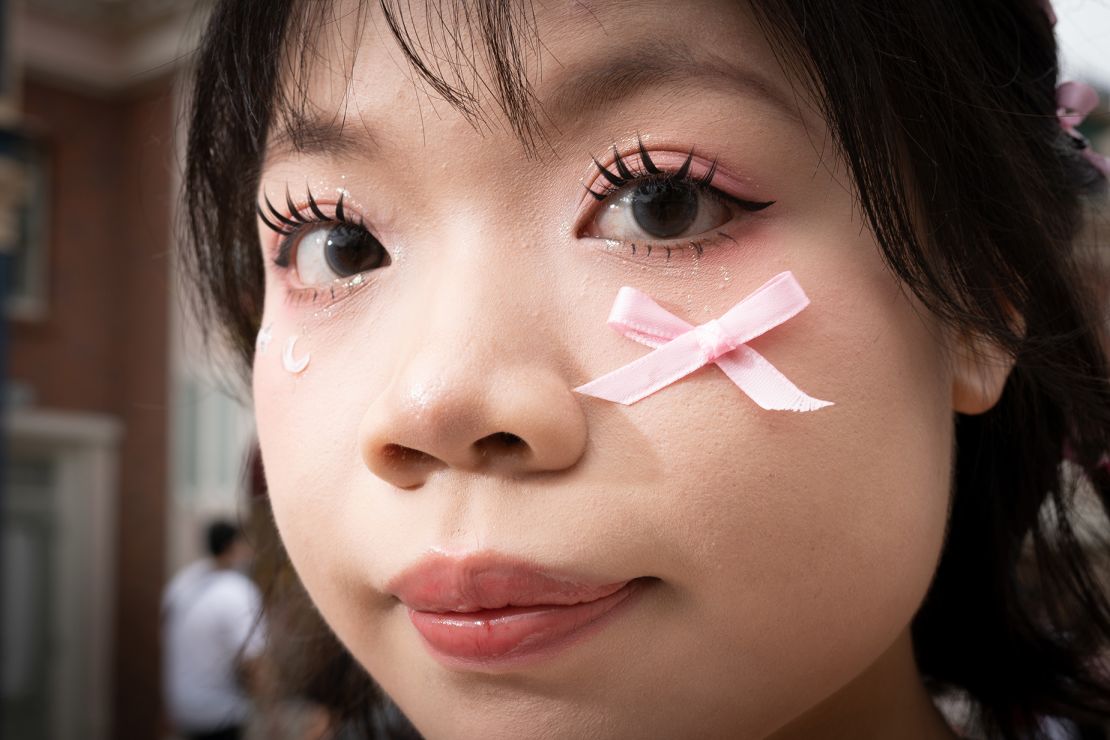 Deng Chundan, 16, poses for a picture during an interview with CNN. She decorated her face with a pink ribbon and face stickers.