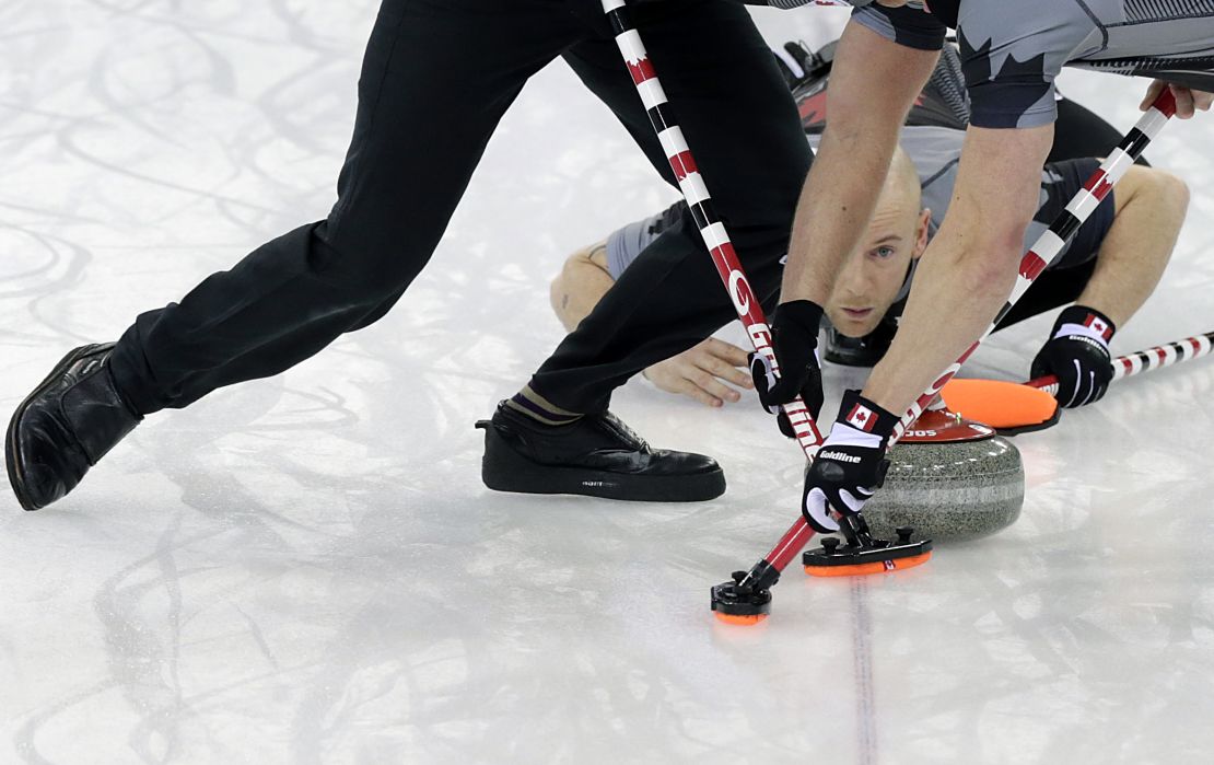 Canada's Ryan Fry delivers the rock while teammates Ryan Harnden (left) and E.J. Harnden (right) sweep the ice during the men's curling gold medal game against Britain at the 2014 Winter Olympics.