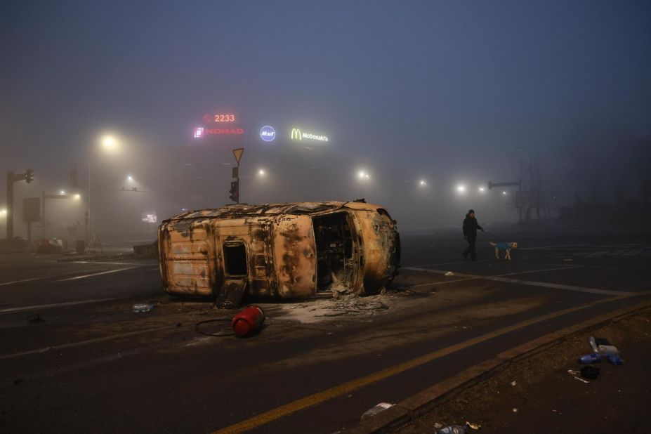 A man walks his dog near a burned-out car in Almaty on January 6.