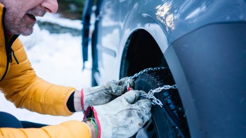 A person puts snow chains on his tire while parked in snowy conditions. 