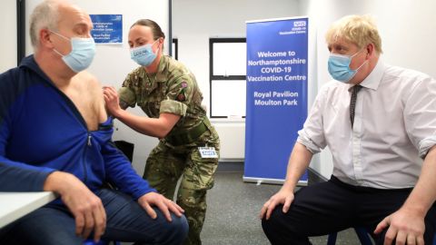 Britain's PM Boris Johnson looks on while Gordon Halfacre receives a vaccine from Cpl. Lorna MacDonald on January 6, 2022 in Northampton, England.