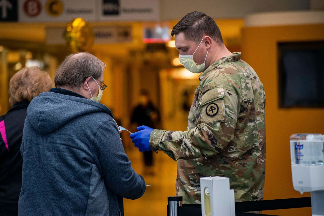 A soldier helps welcome visitors in the lobby handing out new masks and visitor stickers at UMass Memorial Medical Center in Worcester, Massachusetts on December 30, 2021.