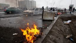 People walk past cars, which were burned after clashes, on a street in Almaty, Kazakhstan, Friday, Jan. 7, 2022. 