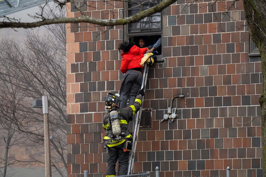 People escape the building through a window as FDNY personnel assist.