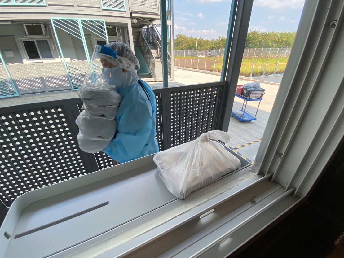 A staff member delivers meals in plastic bags to people who are in quarantine at the camp.