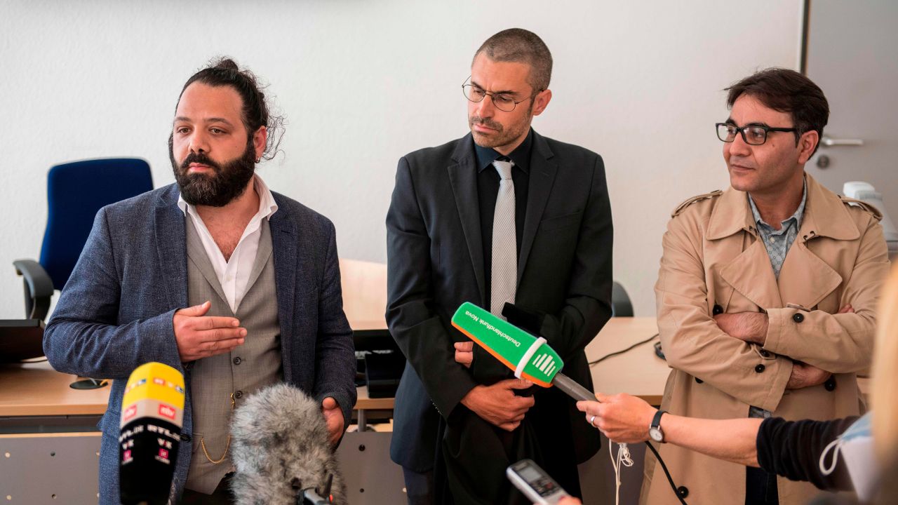 Attorney Patrick Kroker, center, and co-plaintiffs Wassim Mukdad, left, and Hussein Ghrer, right, answer journalists' questions outside the courtroom in Koblenz, Germany, at the start of the trial in April 2020.