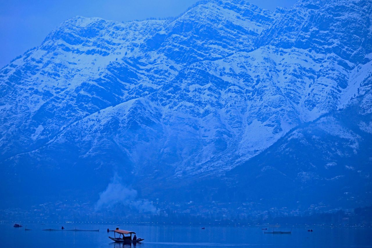 People enjoy a boat ride on Dal Lake, near snow-covered mountains in Srinagar, India, on Tuesday, January 11.